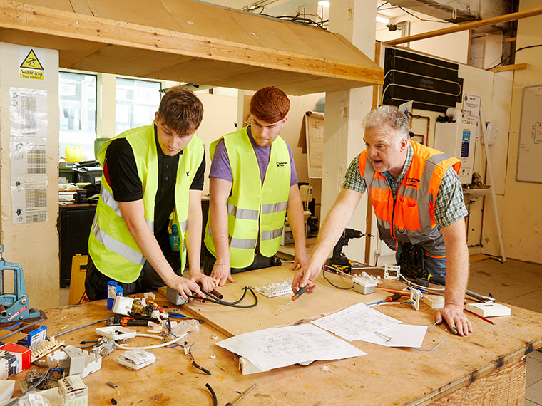 Two plumbing students being supported by their tutor