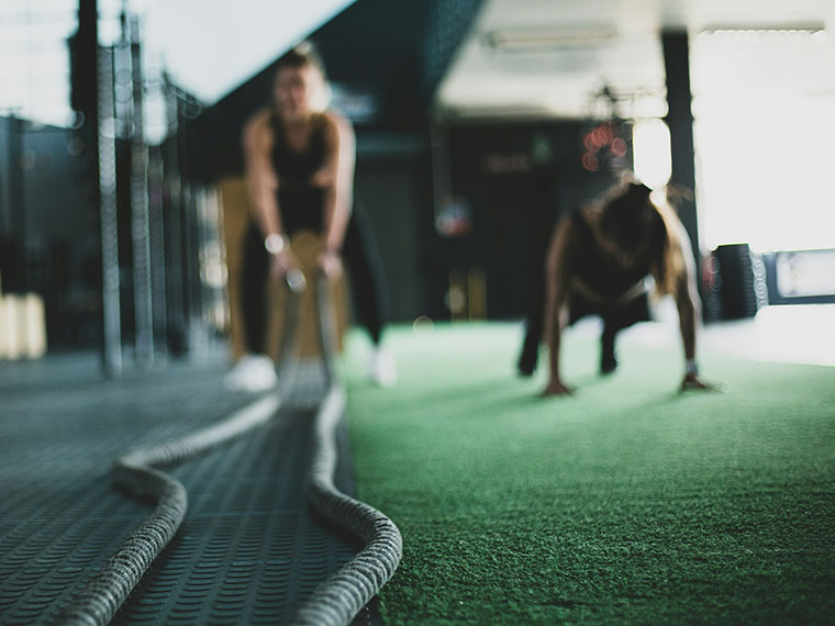 A blurred image of two people in the gym, one using equipment and the other in a plank position